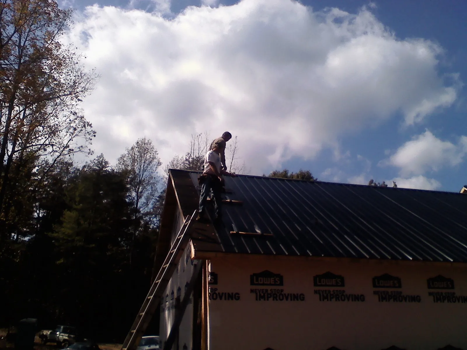 Roofer fastening dark metal panels high against a cloudy sky, from a Roof Inspection job in Fairhope