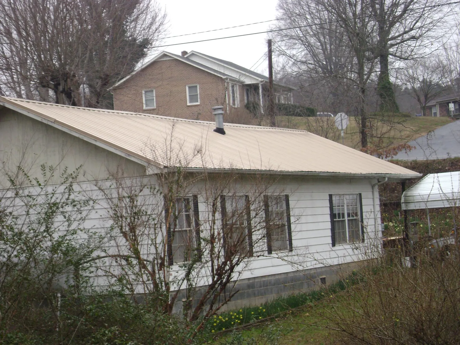 Tan metal roof on a white sided house set into a hillside — Commercial Roofing by Roofing Brothers in Fairhope