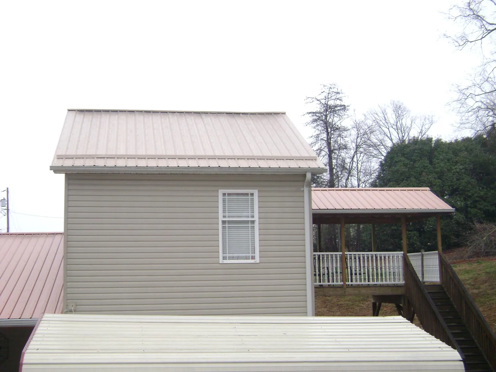 Tan metal roofs on a two story addition and attached porch, from a Roof Replacement job in Fairhope